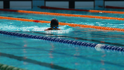 Young swimmer with black swimming cap swims breaststroke in the swimming pool for competition