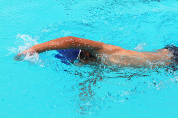 Young man swimmer with blue cap swims front crawl or forward crawl stroke in a swimming pool for competition or race