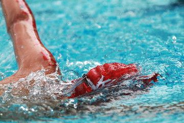 Fototapeta na wymiar Close up young boy swimmer with red cap swim free style or forward crawl in a swimming pool for competition or race