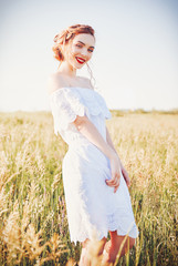Fototapeta na wymiar Portrait of cute smiling young woman wearing white dress in field