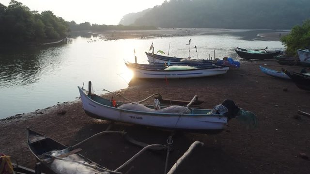 Aerial view. Flight near a wooden boats on the shore with very low altitude and speed. Traditional Indian boats with nets, tackle, gear and flags at sunset. 