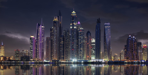 Fototapeta na wymiar Wolkige Skyline von Dubai am Abend mit Wasser-Spieglung