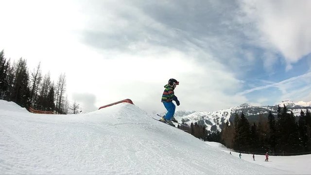 Freestyle skiing. Little boy jumping in a snowpark. A 5 year old child enjoys a winter holiday in the Alpine resort. Stabilized shot. Slow motion.