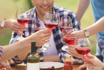 Young people with glasses of wine at table outdoors. Summer barbecue
