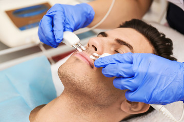 Young man undergoing microcurrent therapy in beauty salon, closeup