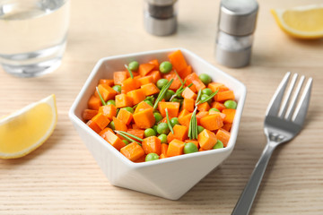 Tasty salad with fresh carrot in bowl on wooden table