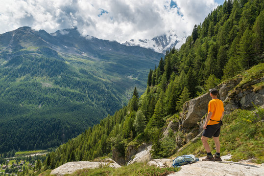 Hiking in the Italian Alps. Hiker with backpack, look at the panorama from above. The village below is Macugnaga and is located at the foot of Monte Rosa (on background), Anzasca valley, Italy