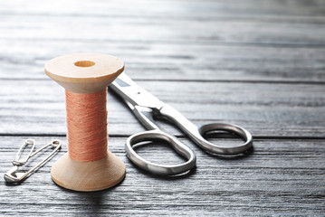Spool of thread, scissors and pins on wooden background. Tailoring equipment
