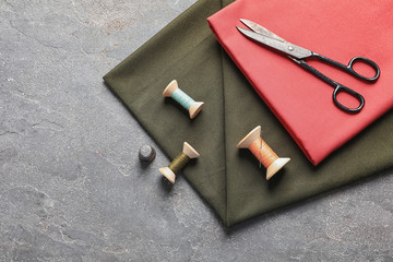 Scissors, threads and fabric on grey background, top view. Tailoring equipment