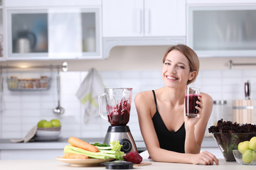 Young woman with glass of tasty healthy smoothie at table in kitchen