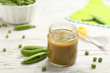 Jar with healthy baby food and green peas on table
