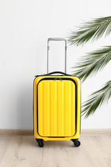Bright yellow suitcase and palm branches near light wall indoors