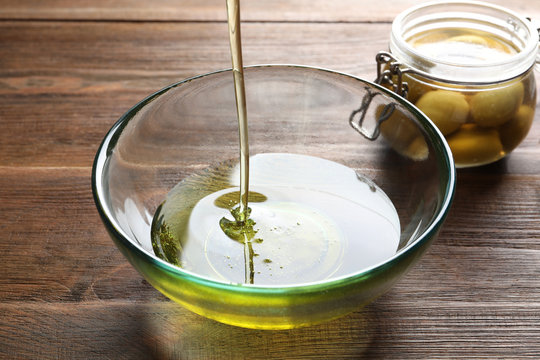 Pouring fresh olive oil into bowl on wooden background