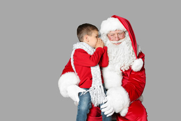 Obraz premium Little boy whispering in authentic Santa Claus' ear on grey background
