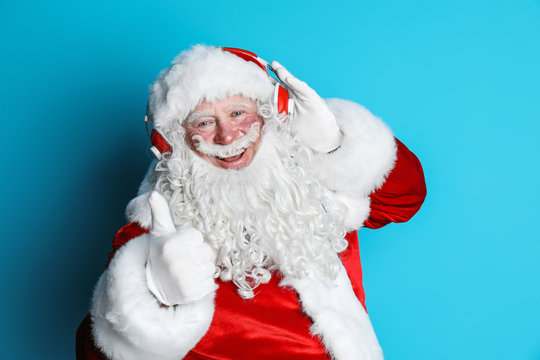 Authentic Santa Claus listening to music on color background