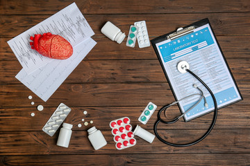 Flat lay composition with stethoscope and pills on wooden background. Cardiology service