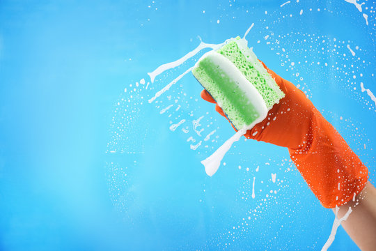 Woman cleaning glass with sponge against color background