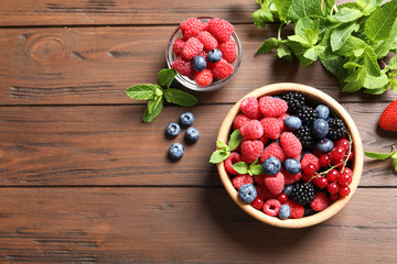 Bowl with raspberries and different berries on wooden table, top view