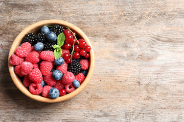 Bowl with raspberries and different berries on wooden table, top view