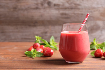 Glass with tasty strawberry smoothie on wooden table