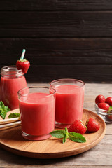 Glasses with tasty strawberry smoothie on wooden plate