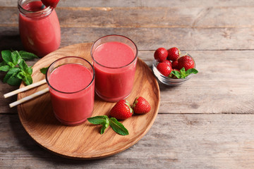 Glasses with tasty strawberry smoothie on wooden plate