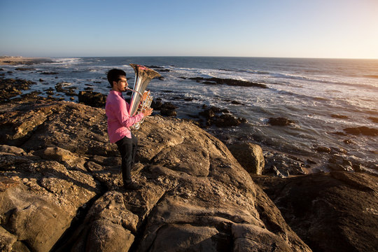 Musician play to Tuba musical instrument on romantic rocky sea shore.