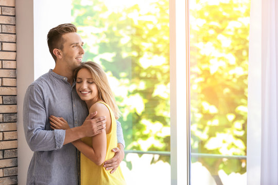 Happy young couple standing near window at home