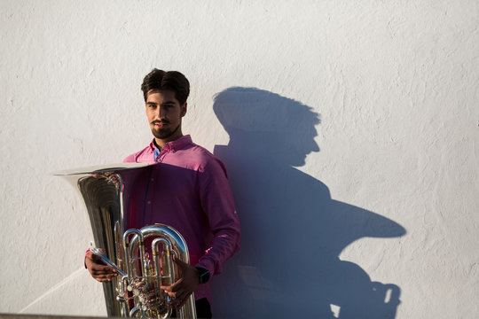 Man with Tuba musical instrument near the white wall the shadow of the tool.
