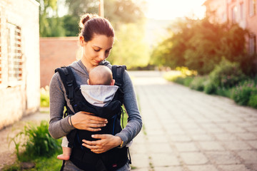 Little baby girl and her mother walking outside during sunset. Mother is holding and tickling her...