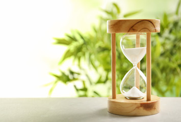 Hourglass with flowing sand on table against blurred background. Time management