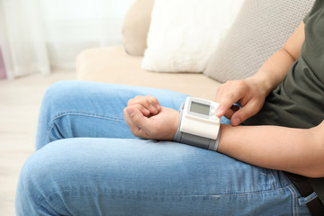 Young man checking pulse with blood pressure monitor on wrist indoors, closeup
