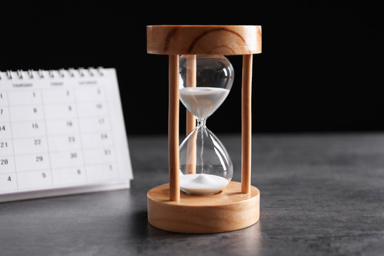 Hourglass and calendar on table against black background. Time management