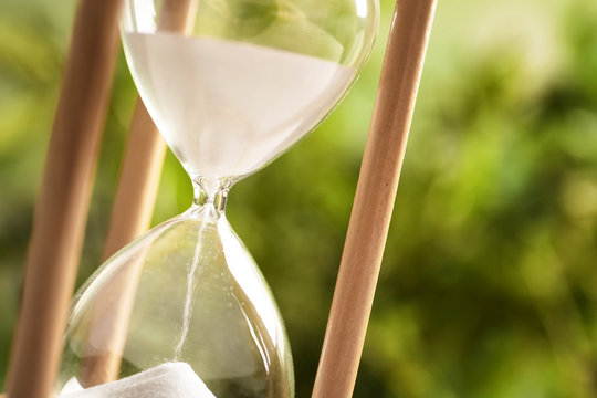Hourglass with flowing sand on blurred background, closeup. Time management