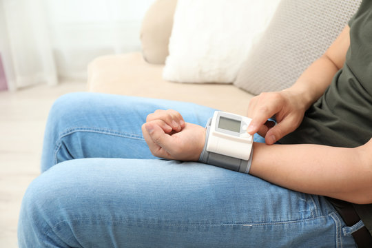 Young Man Checking Pulse With Blood Pressure Monitor On Wrist Indoors, Closeup