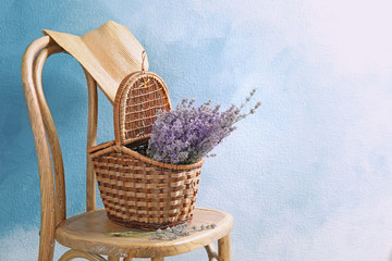 Fototapeta na wymiar Wicker basket with lavender flowers on chair against color background