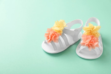 Pair of baby sandals decorated with flowers on color background