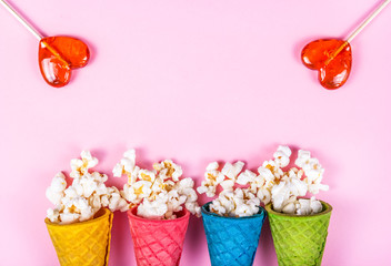 Pink background and sweets. Sparse popcorn and lollipops. Copy space. Popcorn in a waffle cone