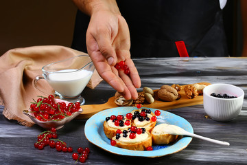 Chef cook sprinkles red berries on crostini sandwiches with ricotta and blueberries on the whole grain bread bruschetta. Rustic food recipe. Close up