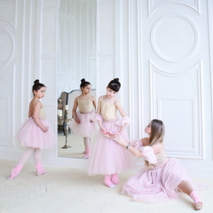 Teacher trains ballet moves with little girls in pink clothes in the room