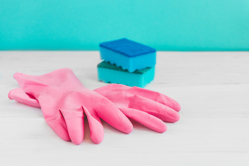 Bottle of dish washing, sponges and pink rubber gloves on white wooden table against a green wall background