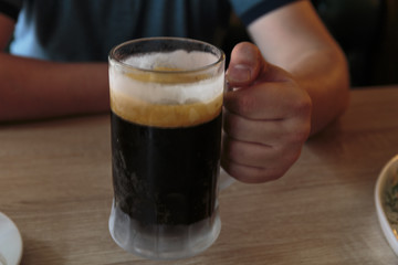 Dark beer in a sweaty mug on wooden table in a hot day.