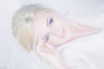 Beautiful bride in white lingerie lies on the bed hidden under the veil