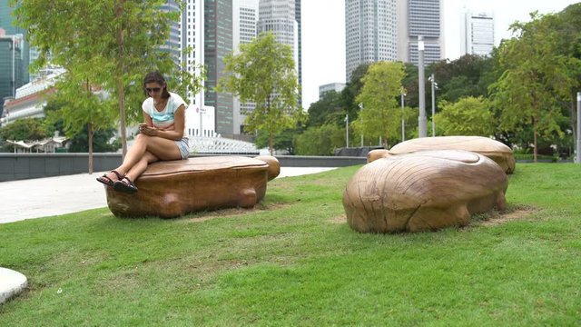 A woman sits on a stone bench in the form of a turtle and uses a smartphone