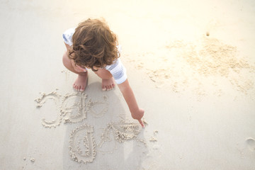 a hairy boy is writing English alphabet on white sand beach