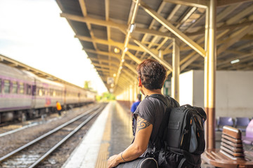 Fototapeta na wymiar a traveller, backpacker man in casual clothes and sunglasses with a camera, sitting and waiting for a train at platform train station