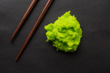 Green wasabi sauce or paste in bowl, with chopsticks or spoon over plain colourful background....