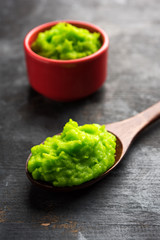 Green wasabi sauce or paste in bowl, with chopsticks or spoon over plain colourful background. selective focus
