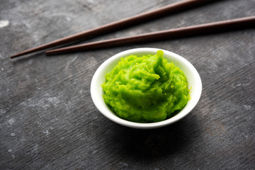 Green wasabi sauce or paste in bowl, with chopsticks or spoon over plain colourful background....