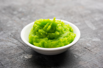 Green wasabi sauce or paste in bowl, with chopsticks or spoon over plain colourful background. selective focus